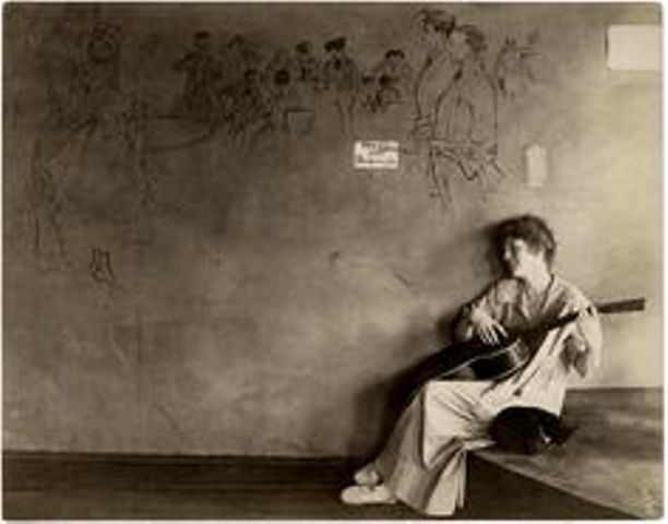 Grace Godwin plays guitar while her cat takes a nap in her tearoom at 58 Washington Square South. The words under the painting on the wall say, "This place ain't bohemian." Could this be Crazy Cat?