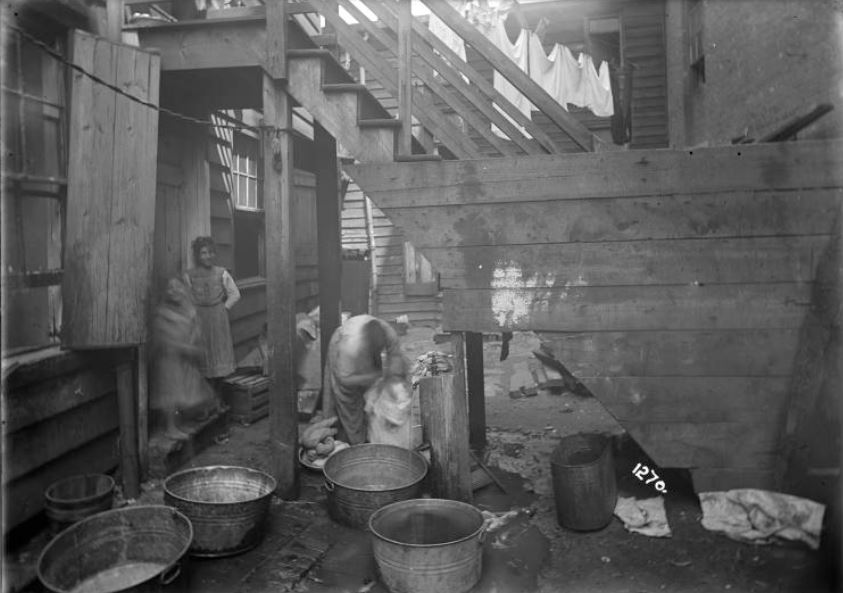 The Tenement House Department employed a staff photographer to provide legal evidence of violations and justify grounds for action. This photo of a woman bathing her children in the rear of a tenement building was taken in 1904. 