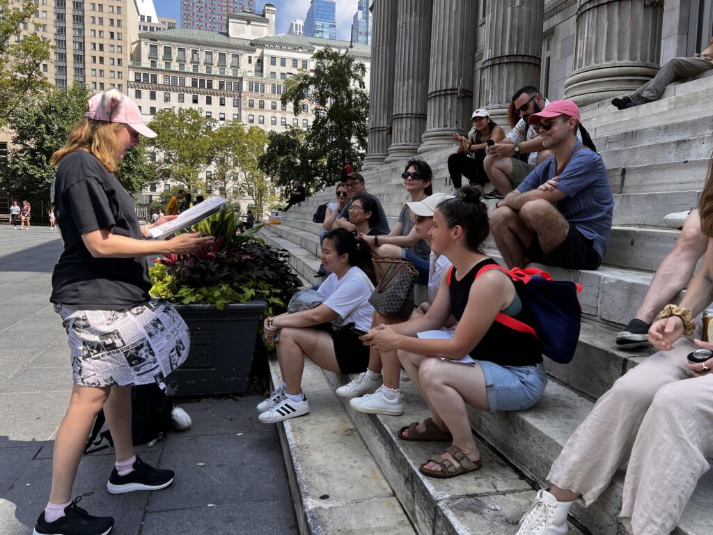 Cats About Town tour guests sit on the steps of Brooklyn Borough Hall as I share the story of hero cat Jerry Fox.